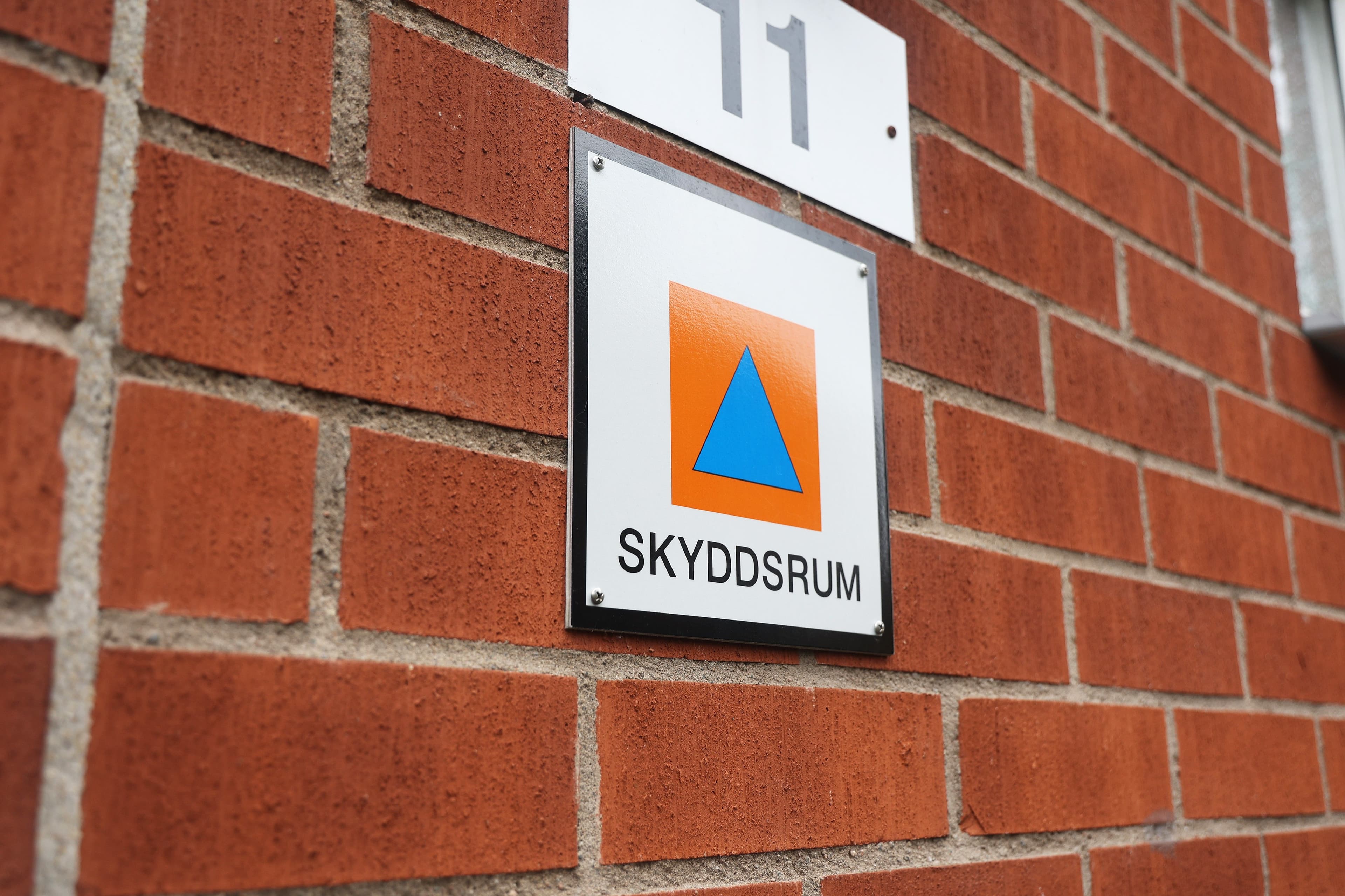Skyddsrumsskylt som markerar ingången till ett skyddsrum på en tegelbyggnad.